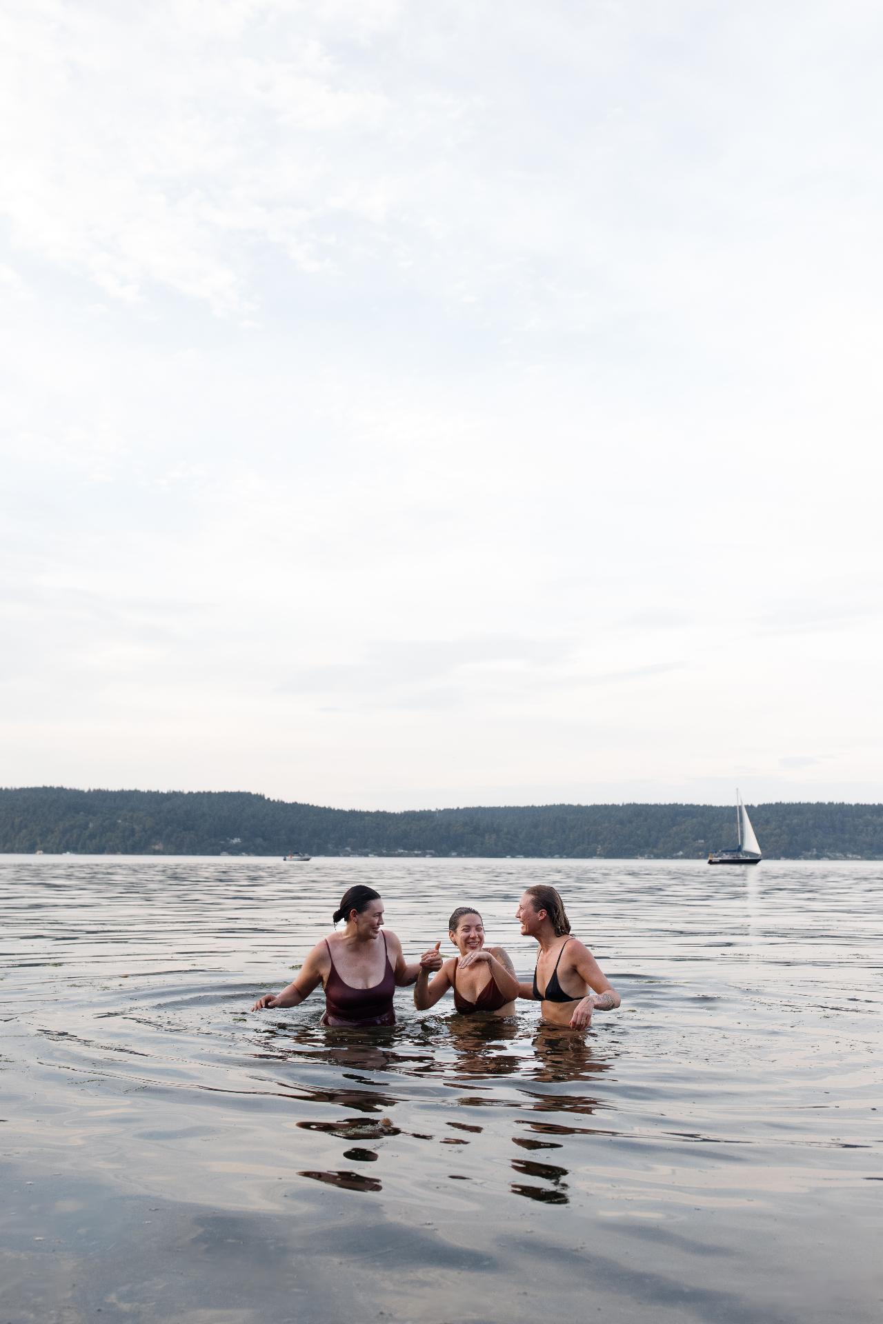 Three Svette guests enjoying a Puget Sound cold plunge with a sailboat in the distance
